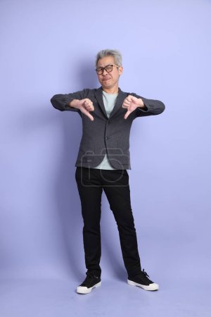 Photo for 50s asian senior Businessman with glasses dressed in formal outfit with gesture of thumbs down isolated on purple background. - Royalty Free Image