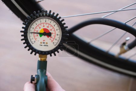 Mano sosteniendo un manómetro de neumático que indica 2.2 bar o 31 psi. Neumático borroso de bicicleta en el fondo. Contexto: inflar neumáticos de bicicleta, aire, monitoreo, seguridad de la bicicleta, servicio.