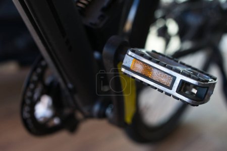 Vista de cerca de un pedal de bicicleta plateado con un reflector naranja y un perfil de goma antideslizante.