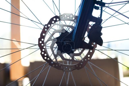 Nahaufnahme des Vorderrades eines E-Bikes mit einer Edelstahl-Bremsscheibe, Bremssattel und einem Teil der dunkelblauen Hochglanzgabel.