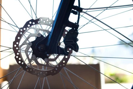 Vue rapprochée de la roue avant d'un vélo électrique, présentant un disque de frein en acier inoxydable, un étrier de frein et une section de la fourche brillante bleu foncé.