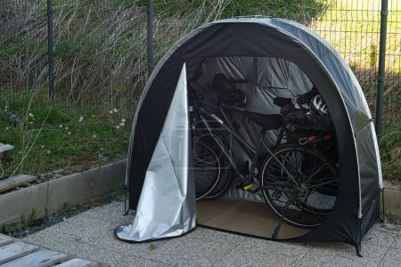 Tente à vélos abritant deux vélos électriques dans une enceinte extérieure. Contexte : local à vélos, sécurité à vélo, place de parking, randonnée à vélo, protection des vélos, excursion, aventure à vélo, camping.