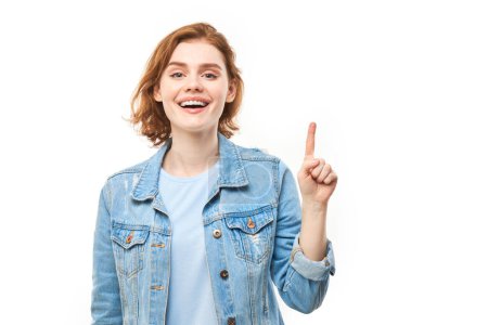 Photo for Portrait of positive redhead young woman in casual jeans smiling pointing with finger at empty copy space for text or product isolated on white background, advertising banner - Royalty Free Image