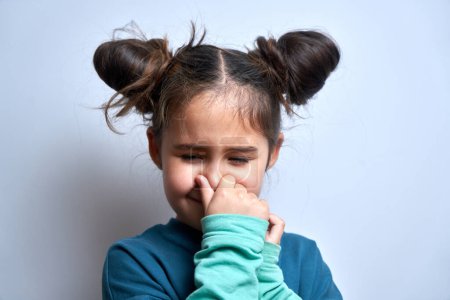 Téléchargez les photos : Petite fille tenant le nez pour éviter l'odeur dégoûtante, pince le nez avec les doigts et retenant le souffle isolé sur fond blanc - en image libre de droit