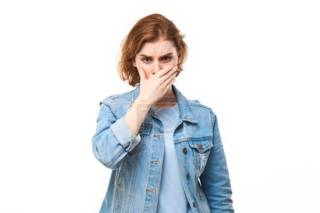 Foto de Mujer joven pelirroja sosteniendo la nariz para evitar el olor asqueroso, pellizca la nariz y la boca con los dedos y mantiene la respiración aislada sobre un fondo blanco - Imagen libre de derechos
