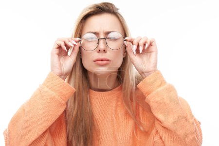 Foto de Mujer joven rubia con gafas entrecerrando los ojos mientras mira la cámara aislada sobre fondo blanco. Concepto problemas de visión - Imagen libre de derechos