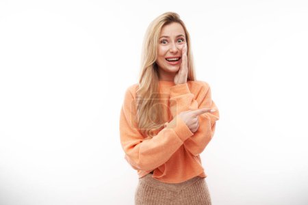 Foto de Chica rubia alegre en naranja casual sonriente señala el dedo en el espacio de copia vacío para texto o producto aislado sobre fondo blanco, banner publicitario - Imagen libre de derechos