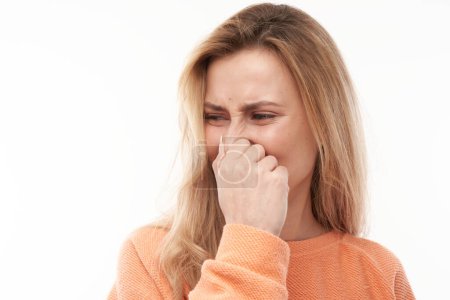 Foto de Mujer rubia joven sosteniendo la nariz para evitar el olor asqueroso, pellizca la nariz y la boca con los dedos y mantiene la respiración aislada sobre un fondo blanco - Imagen libre de derechos