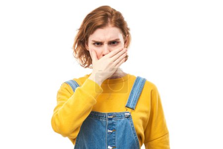 Foto de Mujer joven pelirroja sosteniendo la nariz para evitar el olor asqueroso, pellizca la nariz y la boca con los dedos y mantiene la respiración aislada sobre un fondo blanco - Imagen libre de derechos