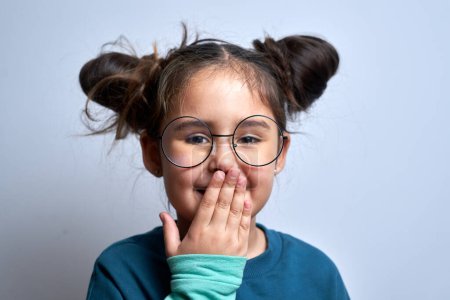 Téléchargez les photos : Petite fille caucasienne surprise couvre sa bouche avec sa paume isolée sur fond blanc - en image libre de droit
