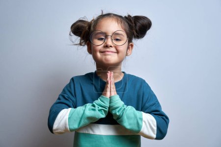 Foto de Retrato de una niña caucásica dobló sus manos en gesto de oración aislado sobre fondo blanco. Concepto pacífico, agradecido y confiado - Imagen libre de derechos