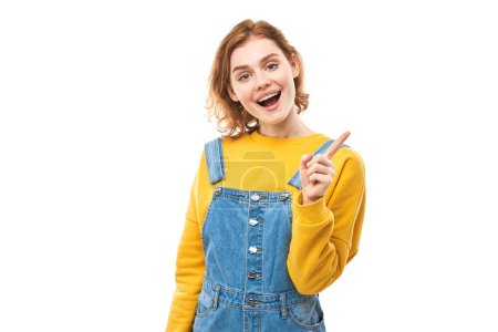 Téléchargez les photos : Portrait de jeune femme rousse positive en jean décontracté souriant pointant du doigt l'espace de copie vide pour le texte ou le produit isolé sur fond blanc, bannière publicitaire - en image libre de droit