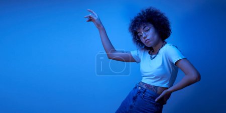 Photo for Portrait of cool kazakh girl with curls and tattoo dancing and posing in neon light isolated on studio background - Royalty Free Image