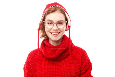 Téléchargez les photos : Portrait de jolie fille aux cheveux roux en pull de Noël rouge et chapeau souriant joyeusement isolé sur fond de studio blanc - en image libre de droit