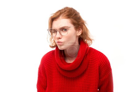 Foto de Mujer joven pelirroja con gafas entrecerrando los ojos mientras mira la cámara aislada sobre fondo blanco. Concepto problemas de visión - Imagen libre de derechos