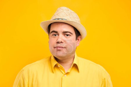 Foto de Retrato del hombre gordo positivo en sombrero sonriendo amablemente aislado en el fondo del estudio amarillo, concepto de vacaciones de viaje - Imagen libre de derechos
