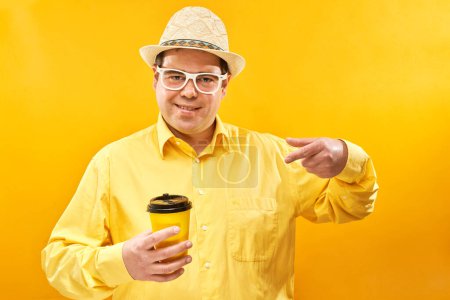 Foto de Enérgico hombre divertido sosteniendo y bebiendo una taza de café para llevar, sonriendo y disfrutando de una bebida aislada sobre un fondo amarillo - Imagen libre de derechos