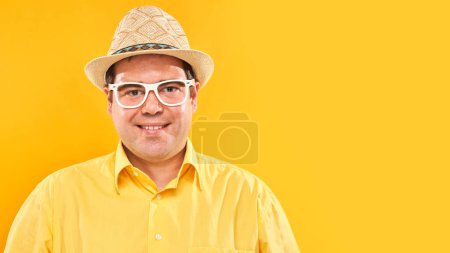 Foto de Retrato del hombre gordo positivo en sombrero sonriendo amablemente aislado en el fondo del estudio amarillo, concepto de vacaciones de viaje - Imagen libre de derechos