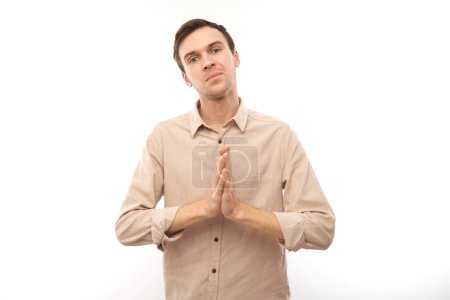 Téléchargez les photos : Portrait de jeune homme brune plié les mains dans un geste de prière isolé sur fond blanc. Paisible, reconnaissant, confiant, fait un concept de souhait - en image libre de droit