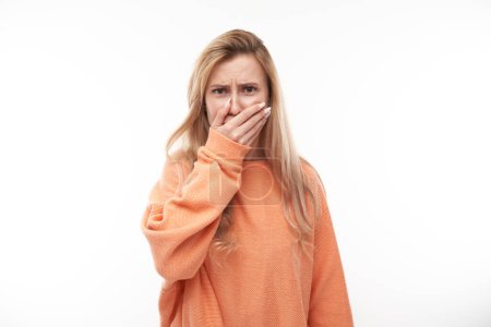 Photo for Young blonde woman holding nose to avoid disgusted smell, pinches nose and mouth with fingers and holding breath isolated on white background - Royalty Free Image