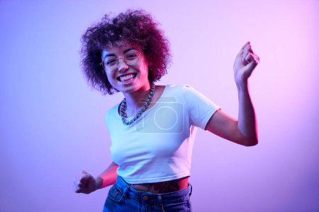 Photo for Portrait of cool kazakh girl with curls and tattoo dancing and posing in neon light isolated on studio background - Royalty Free Image