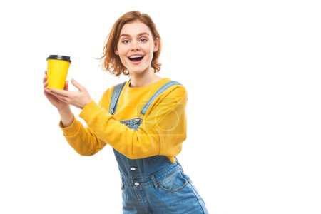 Photo for Energetic redhead girl holding and drinking yellow cup of takeaway coffee, smiling and enjoying drink isolated on white background - Royalty Free Image
