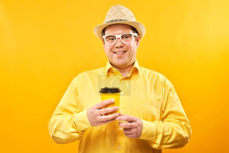 Photo for Energetic funny man holding and drinking cup of takeaway coffee, smiling and enjoying drink isolated on yellow background - Royalty Free Image