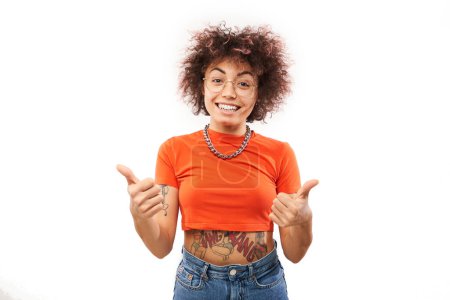 Photo for Kazakh brunette girl with tattoo shows hand with thumbs up and smiles at the camera isolated on white background - Royalty Free Image