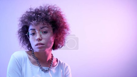 Photo for Close-up face portrait of cool kazakh model girl with curls and chain in neon light isolated on studio background - Royalty Free Image