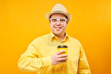 Téléchargez les photos : Homme drôle énergique tenant et buvant une tasse de café à emporter, souriant et savourant une boisson isolée sur fond jaune - en image libre de droit