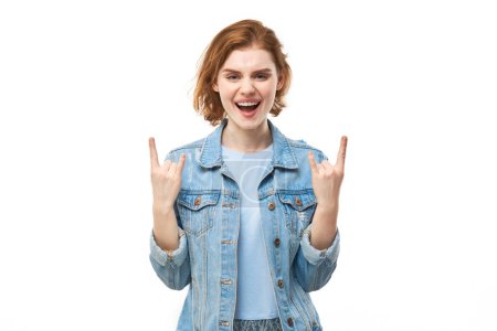 Téléchargez les photos : Portrait de jeune femme rousse montrant un geste rock and roll avec les doigts isolés sur fond blanc - en image libre de droit