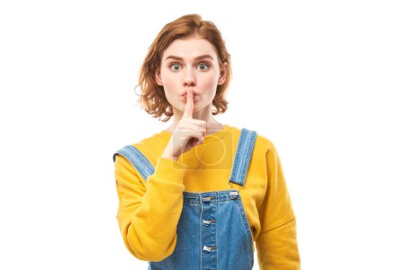 Photo for Portrait of young redhead woman covering mouth with finger isolated on white background. Asks for silence, keep secret, shh gesture - Royalty Free Image
