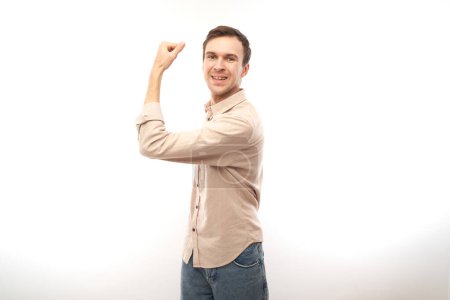 Photo for Portrait of young caucasian man showing biceps, demonstrating power isolated on white background. - Royalty Free Image