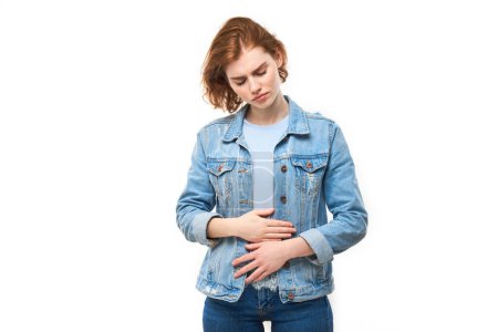 Téléchargez les photos : Portrait de jeune femme tenant la main sur le ventre, souffrant de douleurs menstruelles et d'inconfort intestinal isolé sur fond blanc - en image libre de droit
