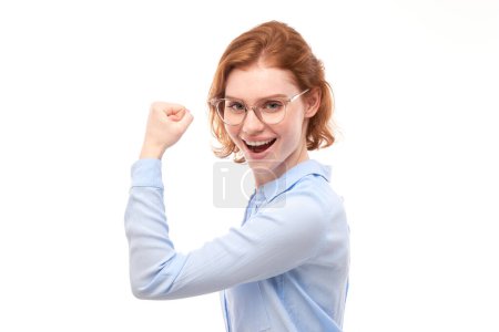 Téléchargez les photos : Portrait de jeune femme aux cheveux roux montrant des biceps, démontrant la puissance de la fille isolée sur fond blanc. - en image libre de droit
