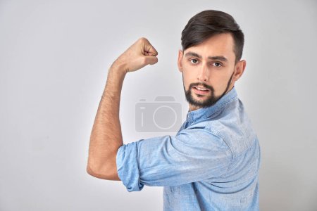 Foto de Retrato de un joven caucásico mostrando bíceps, demostrando poder aislado sobre fondo blanco. - Imagen libre de derechos