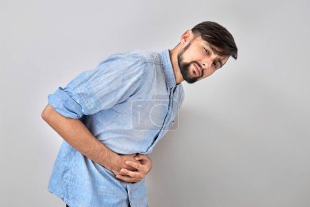 Photo for Portrait of young man holding hands on his stomach, suffering from pain and intestines discomfort isolated on white background - Royalty Free Image