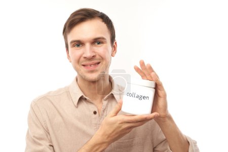 Photo for Portrait of young handsome caucasian man showing jar of collagen powder in his hands and smiling isolated on studio white background - Royalty Free Image