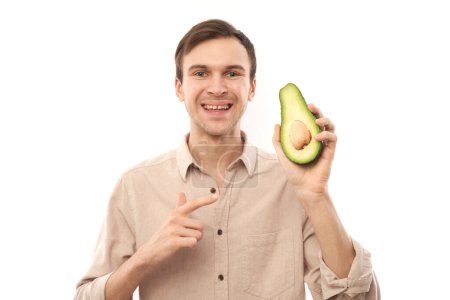 Photo for Portrait of young handsome caucasian brunette man smiling and showing half an avocado isolated on white studio background - Royalty Free Image