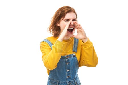 Foto de Retrato de una joven pelirroja gritando en sus palmas sobre fondo blanco del estudio. Información importante, concepto de noticias - Imagen libre de derechos