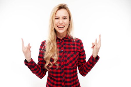Téléchargez les photos : Portrait de jeune femme blonde montrant un geste rock and roll avec les doigts isolés sur fond blanc - en image libre de droit