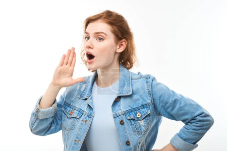 Foto de Retrato de una joven pelirroja gritando en sus palmas sobre fondo blanco del estudio. Información importante, concepto de noticias - Imagen libre de derechos
