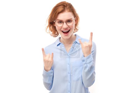 Téléchargez les photos : Portrait de jeune femme rousse montrant un geste rock and roll avec les doigts isolés sur fond blanc - en image libre de droit