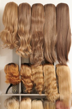 Photo for Showcase of natural looking wigs in different colors fixed on the metal wig holders in beauty salon. Row of mannequin heads with variation shades hair on shelf in wig sho - Royalty Free Image
