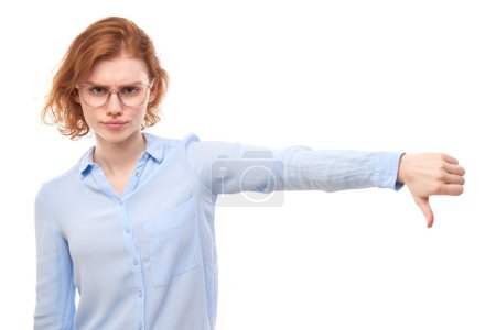 Photo for Portrait of displeased young redhead woman showing thumbs down isolated on white studio background. Does not approve of something, puts a dislik - Royalty Free Image