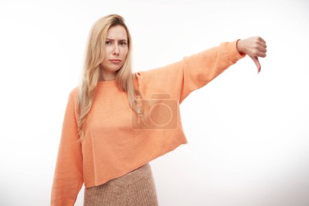 Photo for Portrait of displeased young blond woman showing thumbs down isolated on white studio background. Does not approve of something, puts a dislik - Royalty Free Image