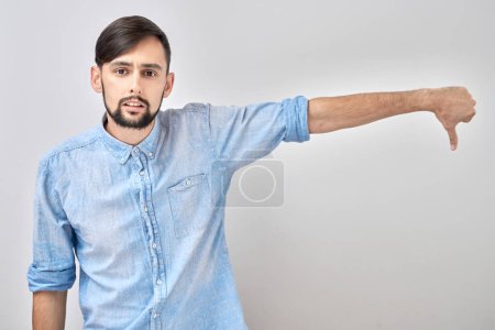 Photo for Portrait of displeased caucasian man showing thumbs down isolated on white studio background. Does not approve of something, puts a dislik - Royalty Free Image