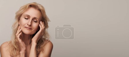 Photo for Beautiful blond middle aged woman smiling touching face closed eyes portrait. Elegant mature lady no makeup 50 years old close-up isolated on white Women's health, cosmetology, skin care - Royalty Free Image