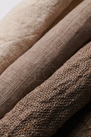 Foto de Ropa de cama en diferentes texturas y colores. Tejidos naturales de lino orgánico y algodón en rollos, textiles hechos a mano. Arpillera y lienzo para decoración ecológica, rústica, boho, hygge - Imagen libre de derechos