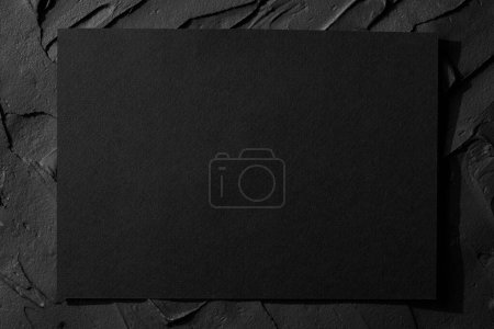Téléchargez les photos : Feuille de carton noir sur fond mural noir texturé mastic. Cadre avec espace de copie vide - en image libre de droit